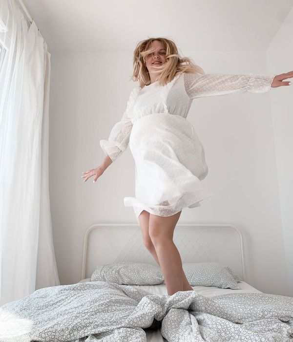 Woman smiling while performing a light cardio movement in a bright, airy room.